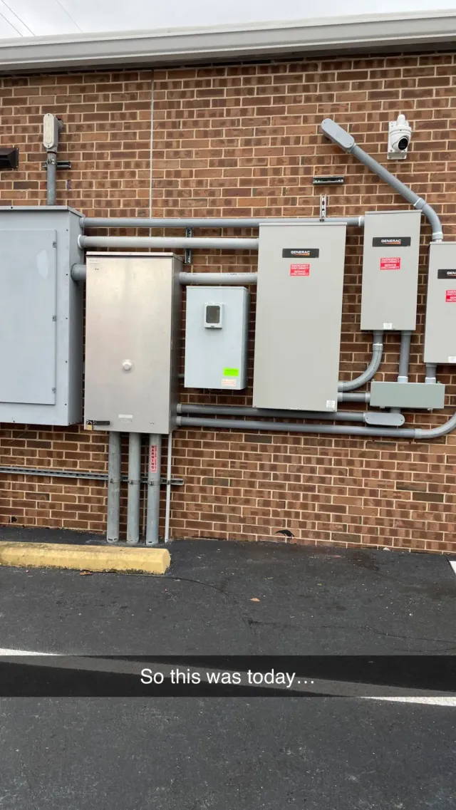 Utility boxes and electrical panels mounted on a brick exterior wall beside a paved surface.