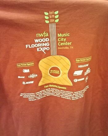 Brown t-shirt with a guitar-shaped graphic promoting the NWFA Wood Flooring Expo at the Music City Center in Nashville.