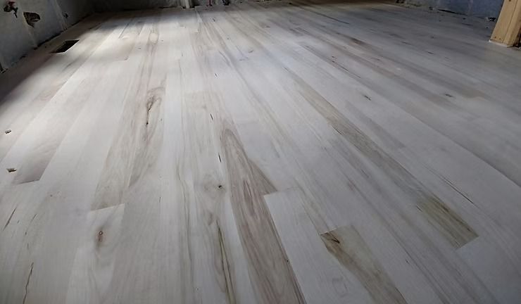 Light-colored hardwood floor with varied grain patterns and some darker streaks, likely newly installed in a room.