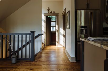 Hallway with wooden floor, railing, refrigerator, and an open door letting in sunlight.
