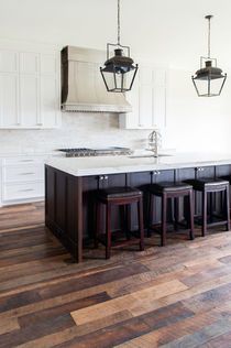 Kitchen with white cabinets, dark island, and wood floors, with hanging lanterns and bar stools.