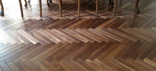 Herringbone pattern hardwood floor under a dining table. The alternating planks have lighter and darker wood tones.