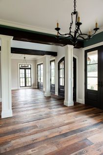 Empty room with rustic wood floors, white columns, black doors, and a chandelier.