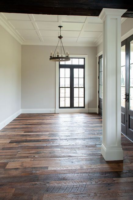 Empty room with wood floors, black-framed windows, white pillars, and a chandelier.