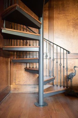 Spiral staircase with wooden steps and metal railing in a room with wood paneling.