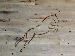 Silhouette of a jumping horse, copper-colored, mounted on a light wood wall.