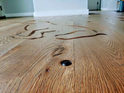 Close-up of light wood floor with dark inlays and a large black hole.