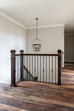 Interior view of a second-story landing with dark wood railing, hardwood floors, and a pendant light.