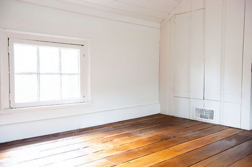 Empty white room with wooden floor, window, and vent.
