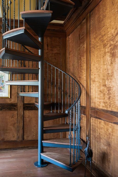 Spiral staircase with dark metal frame and wood steps, set against wood paneling.