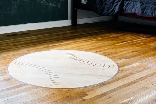 Round wooden baseball-shaped rug on a hardwood floor in a room.