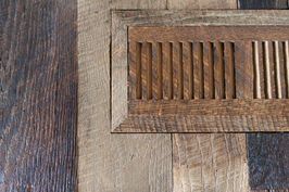 Wooden floor vent with brown vertical slats, surrounded by matching planks.
