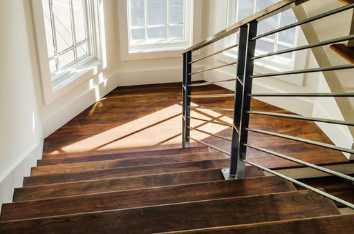 Wooden staircase with metal railing, sunlight streaming in from windows.