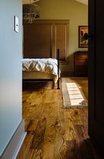 Bedroom interior: hardwood floor, bed with white linens, sunlight streaming in, neutral colors.