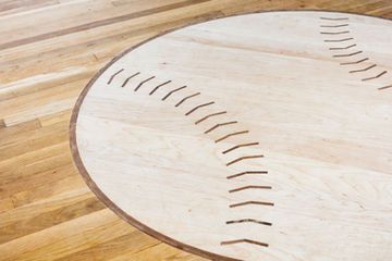 Circular baseball-themed wooden floor inlay: light wood with dark brown stitching and border, set on wood planks.