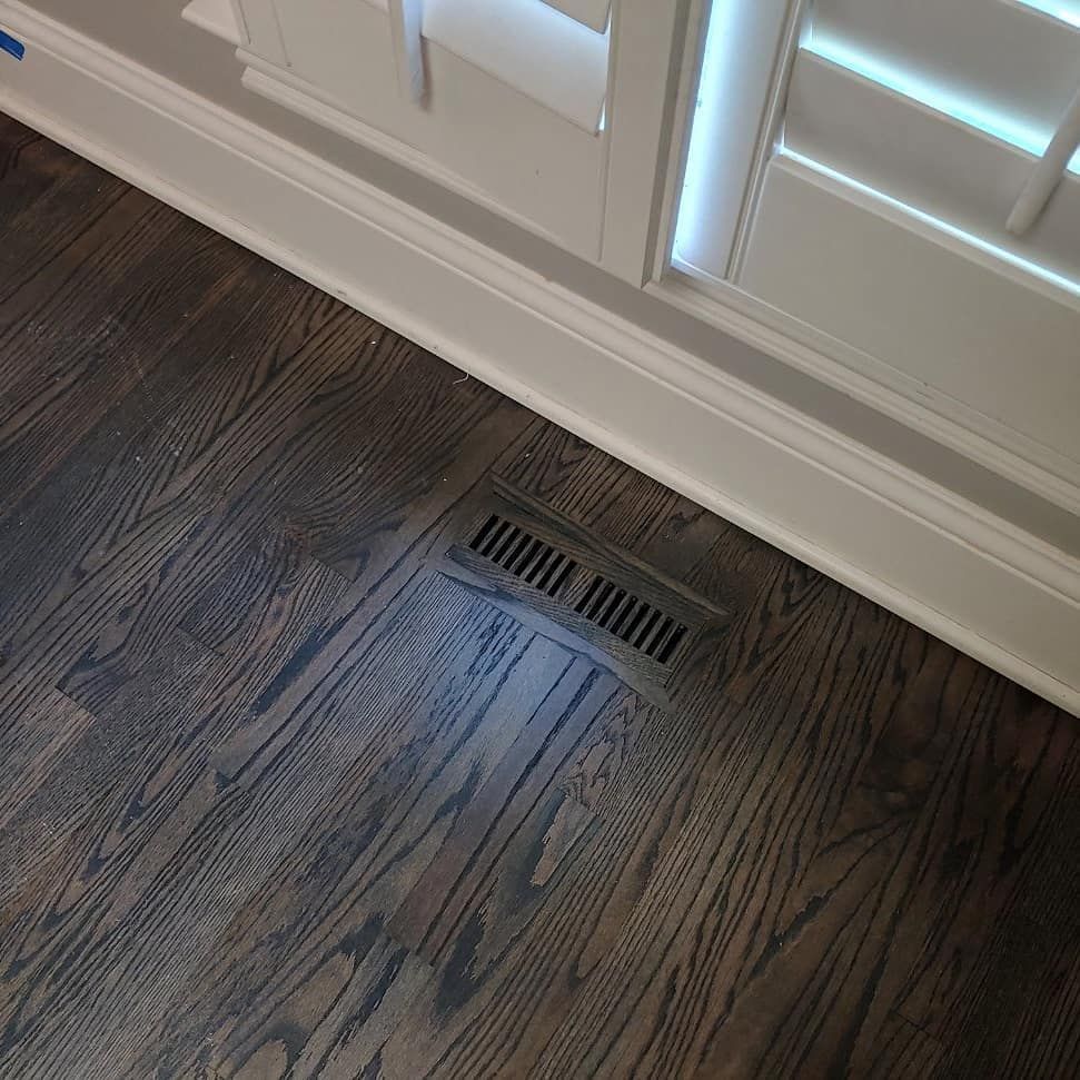 Dark hardwood floor with a floor vent and white trim and shutters.