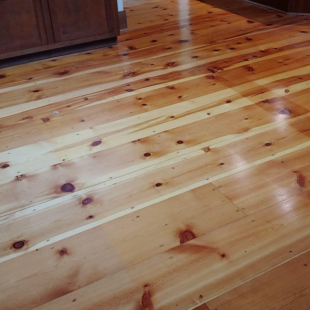 Wooden floorboards with a glossy finish, showing knot details and a textured edge along the boards.