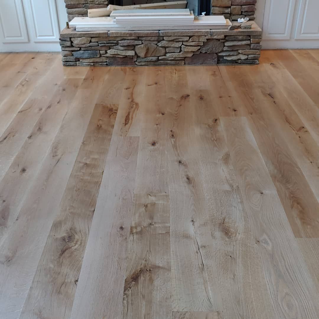 Light wood flooring in front of a stone fireplace, in a home.