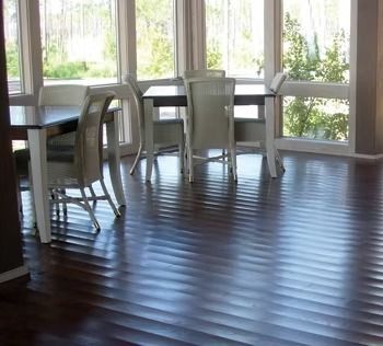 Dark wood floor with ridged pattern in a dining area with white chairs and tables near large windows.