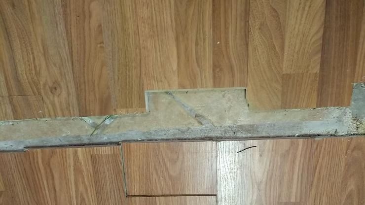 Damaged laminate flooring with exposed subfloor and debris.