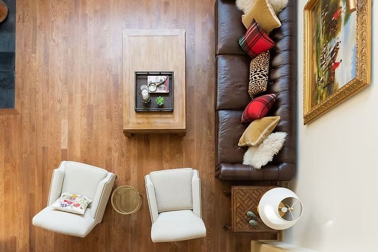 Overhead view of a living room with a brown leather sofa, white chairs, and a wooden coffee table.