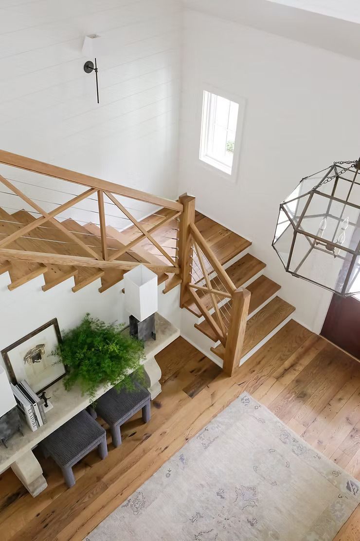 Wooden staircase with decorative railing and a hanging lantern. White walls and wood flooring in a bright, open entryway.