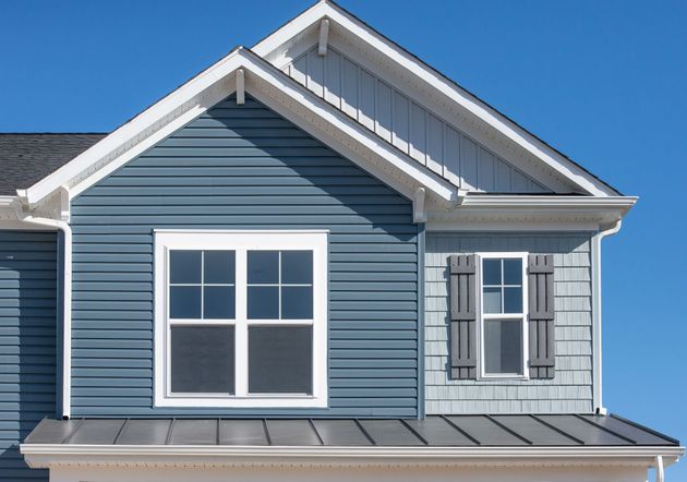 A blue house exterior featuring horizontal siding, a gabled roof, white trim, a large window, and a smaller shuttered window.