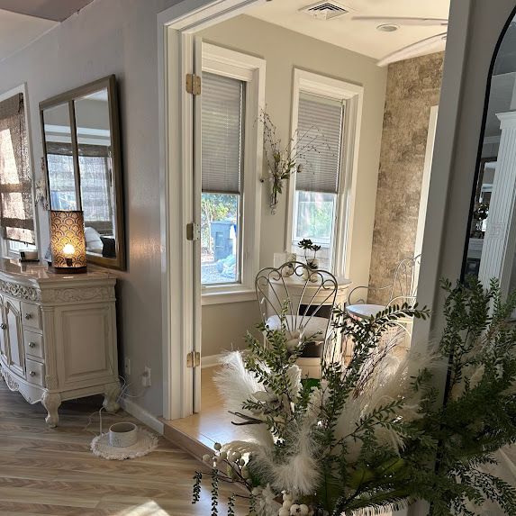 Bright entryway with a white door, mirrors, decorative cabinet, and greenery in the foreground
