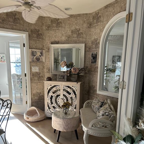 Elegant living room with ornate white cabinet, mirrors, arched window, and neutral upholstered seating