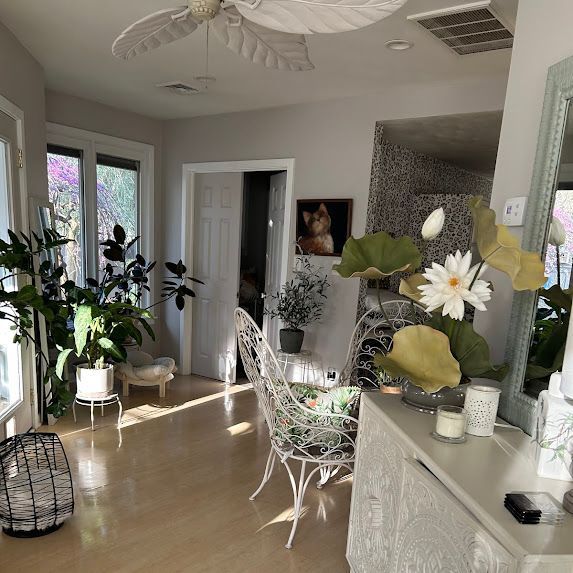 Bright sunroom with plants, white wicker chairs, and floral decor on a light wood floor