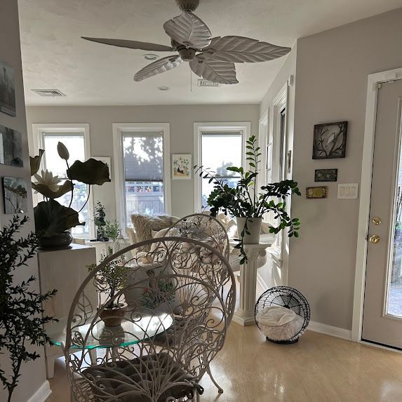 Bright sunroom with wicker chairs, potted plants, large windows, and a ceiling fan.
