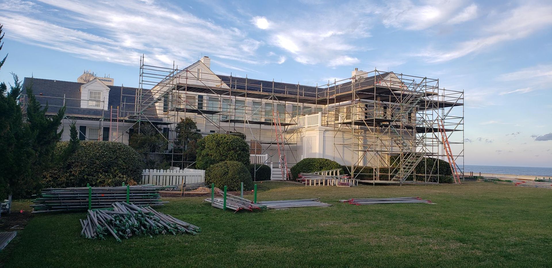 Large stone building under renovation with scaffolding beside a green lawn at sunset