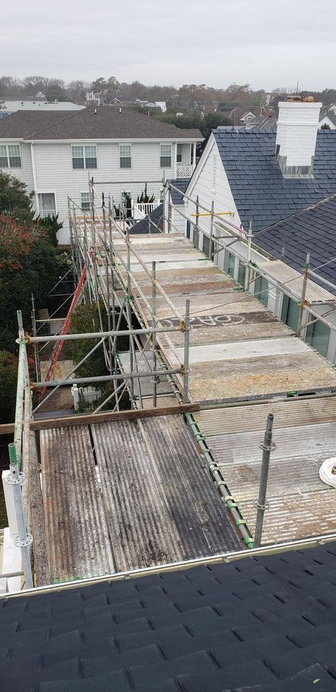 Scaffolded rooftop renovation beside a row of houses under an overcast sky