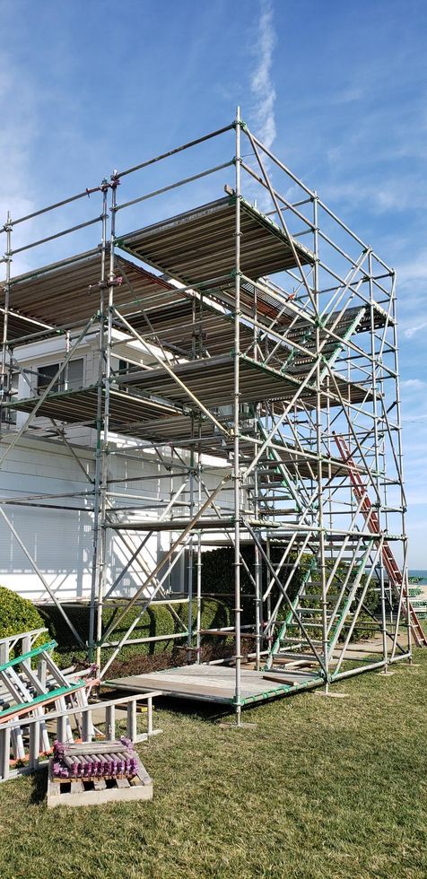 Scaffolding around a multi-level structure outdoors on a grassy lawn under a blue sky