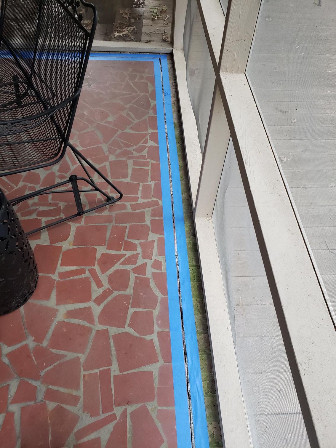 Blue taped border around a red tiled patio beside a light gray wall and black outdoor furniture.