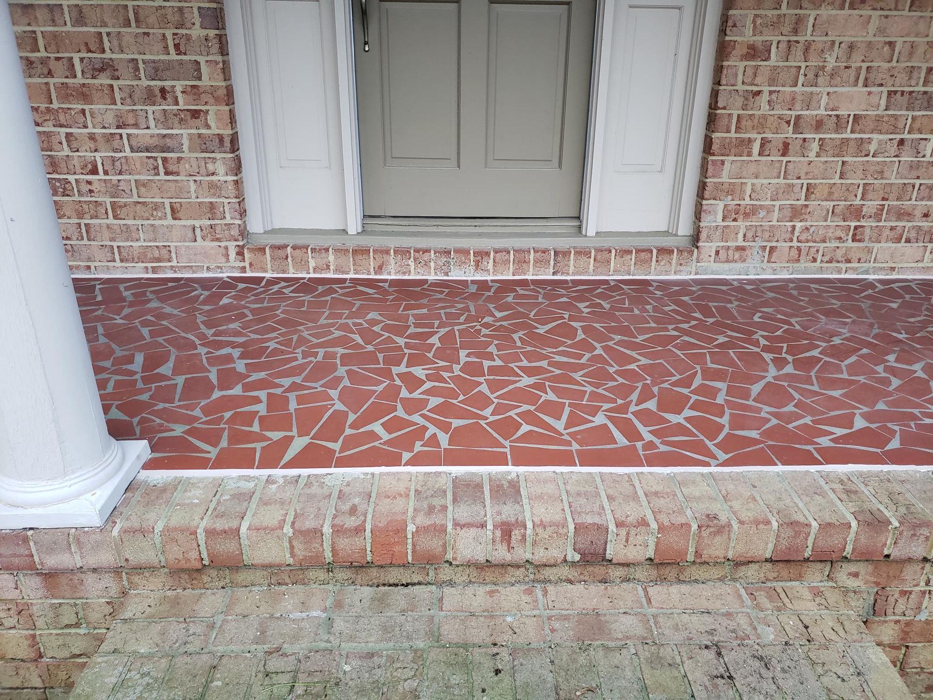 Front porch with red and beige mosaic tile, white columns, and a closed door above a step.
