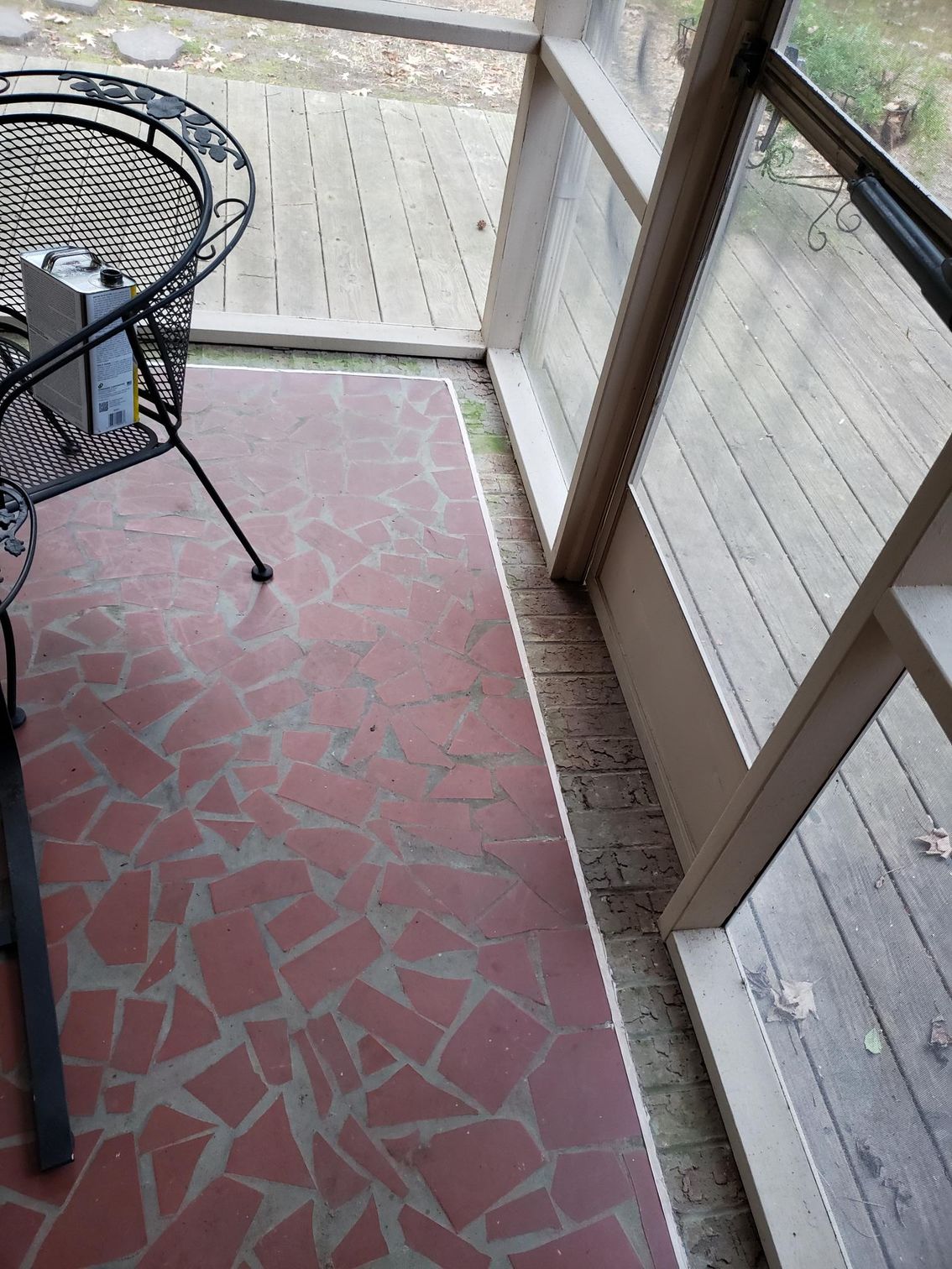 Small balcony with red patterned floor, glass railing, and a metal chair/table.