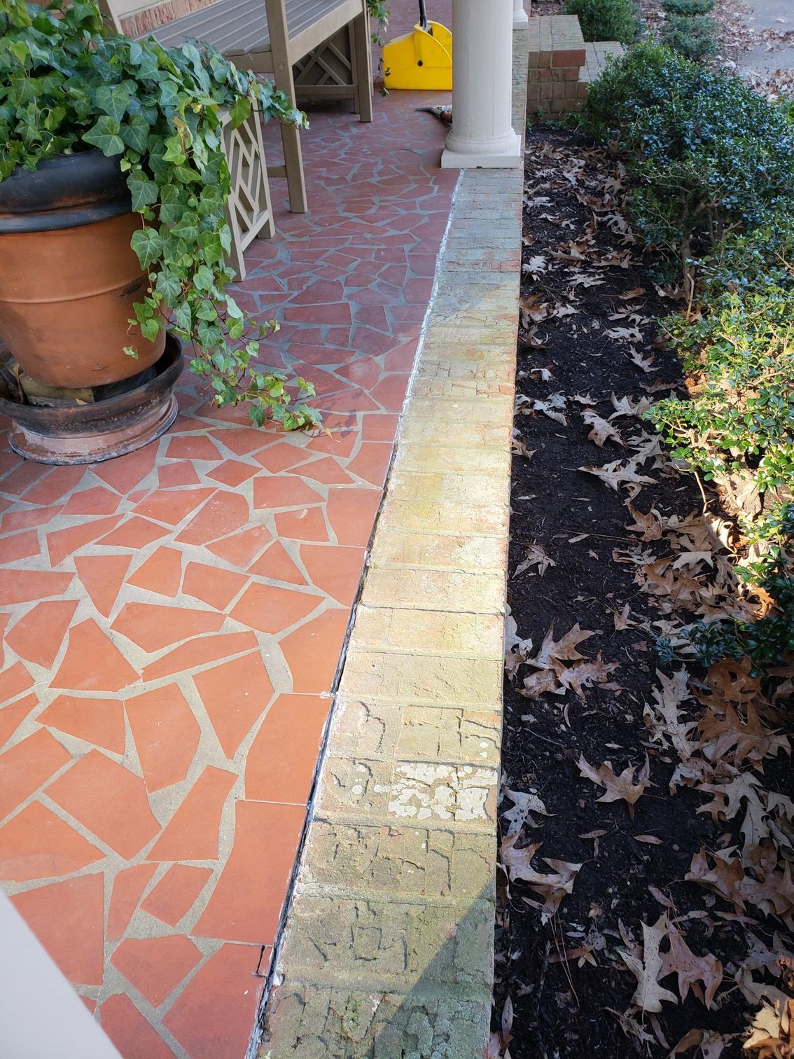 Front porch walkway with red tile, potted plants, and a narrow garden bed along the side.