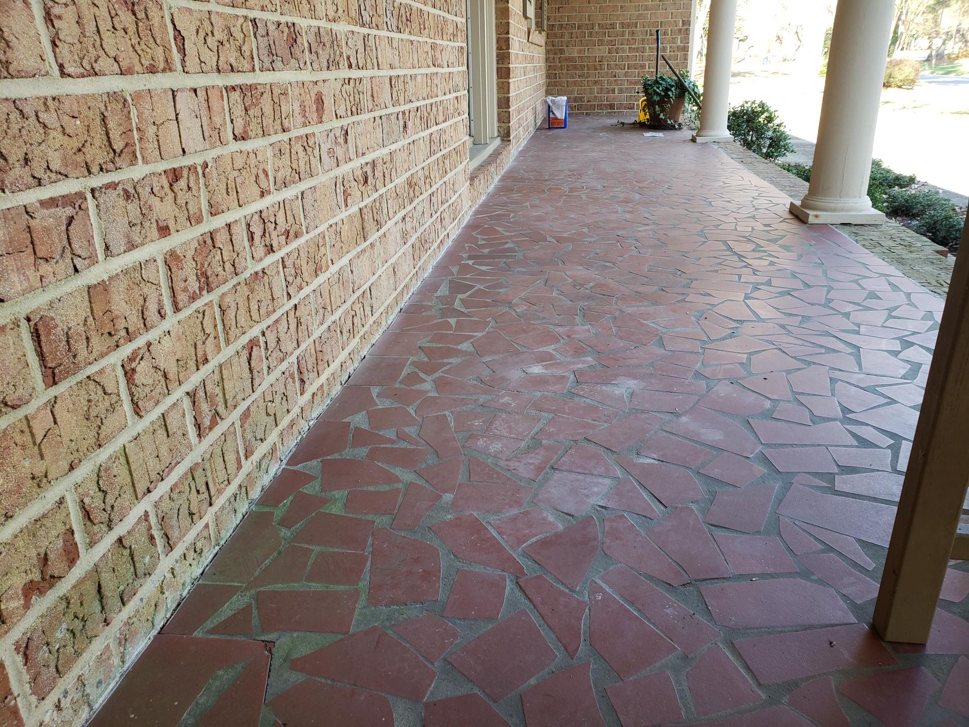 Brick-paved covered walkway beside a tan stone wall and white columns