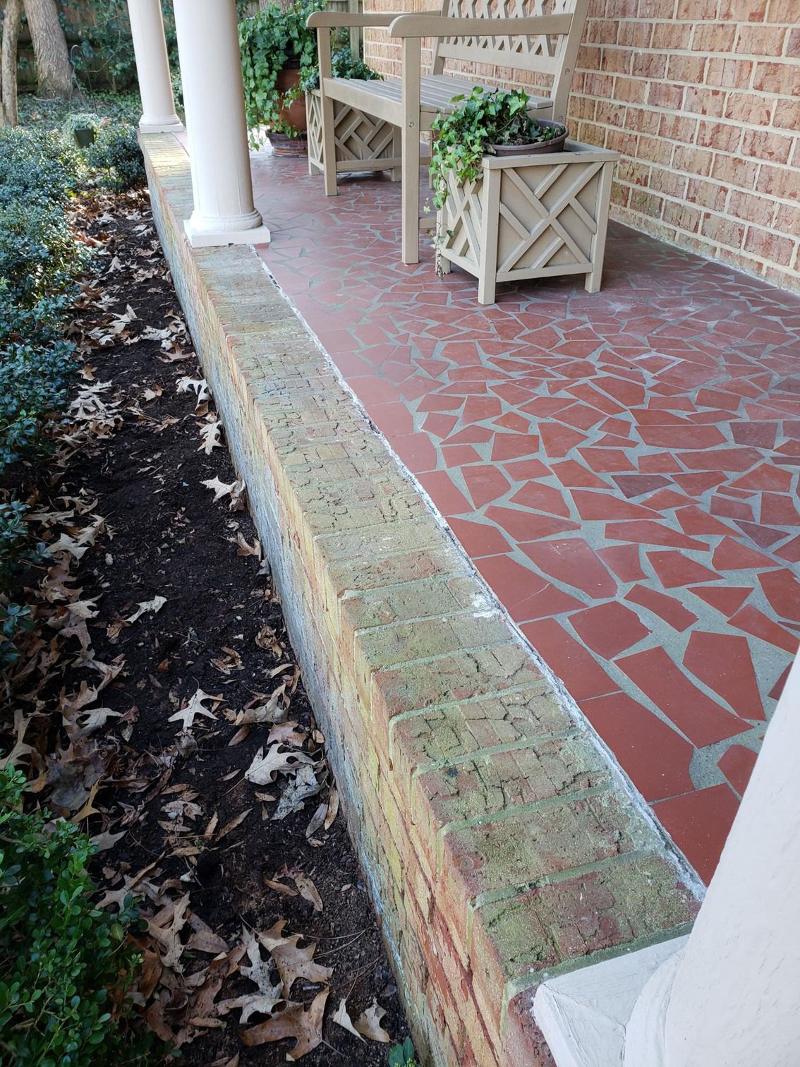 Red-tiled porch with white columns, wooden planters, and a mossy curb beside a leaf-covered walkway