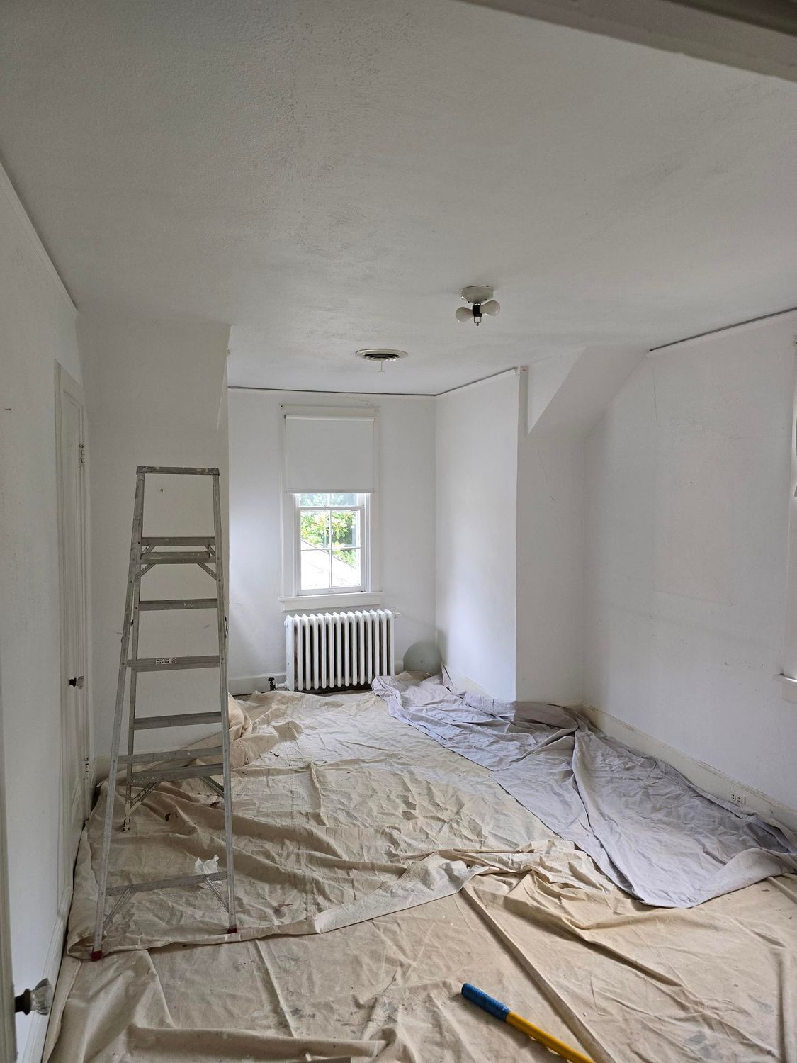 Renovation room with ladder, covered floor, window, radiator, and white walls