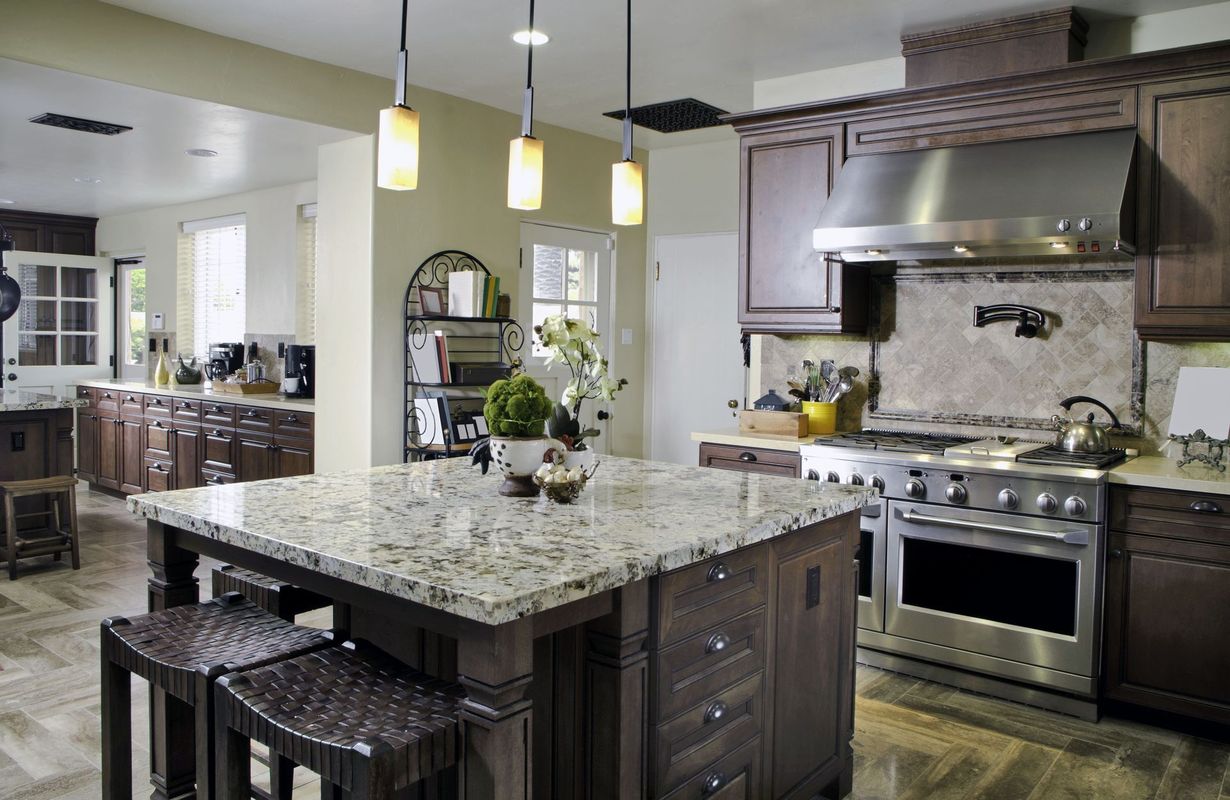 A modern kitchen featuring a granite-topped island with stools, dark wooden cabinets, and stainless steel appliances.