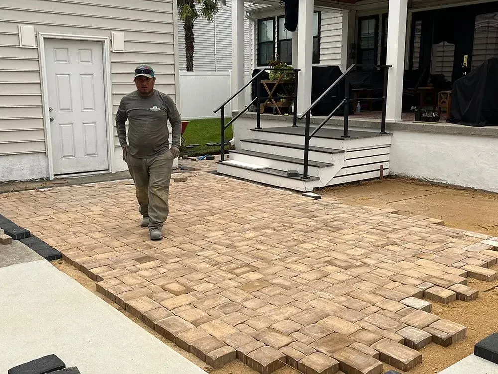 A man is walking on a brick patio in front of a house.
