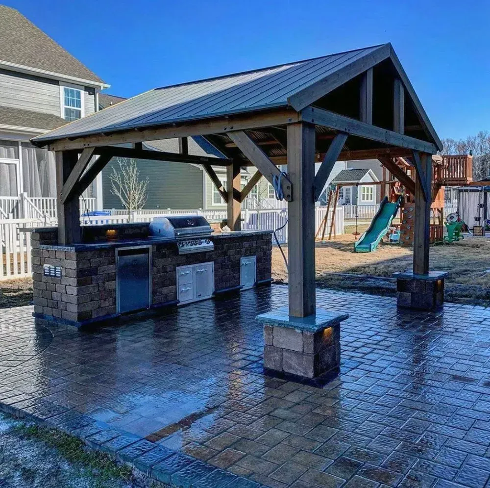 A wooden gazebo with a grill underneath it in a backyard.