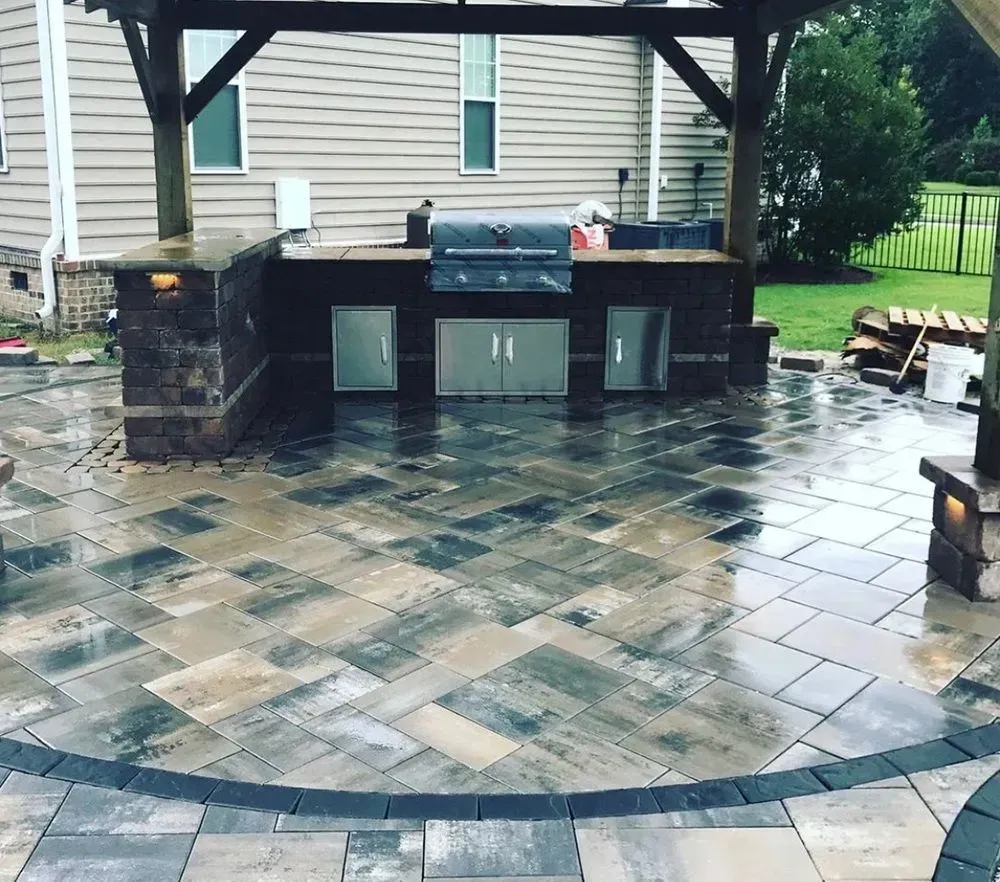 A patio with a grill and cabinets under a pergola.