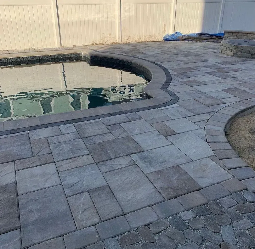 A brick patio next to a swimming pool with a white fence in the background