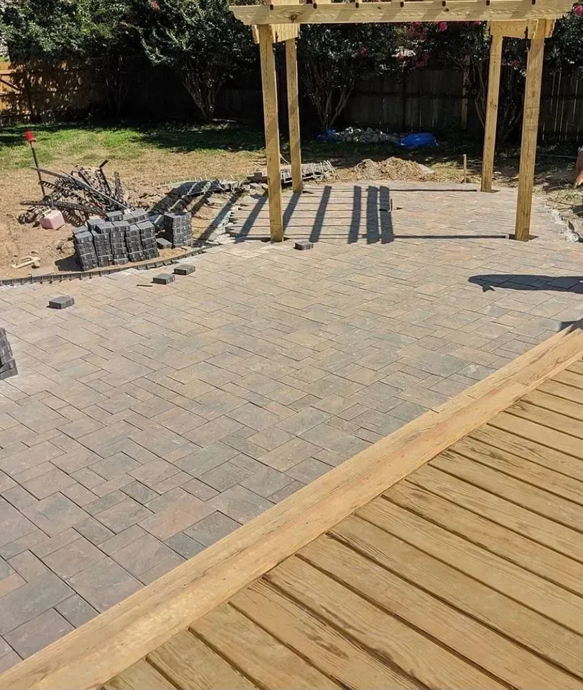 A wooden deck is sitting next to a brick patio with a pergola.