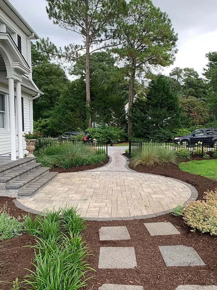 A brick walkway leading to a house with trees in the background.