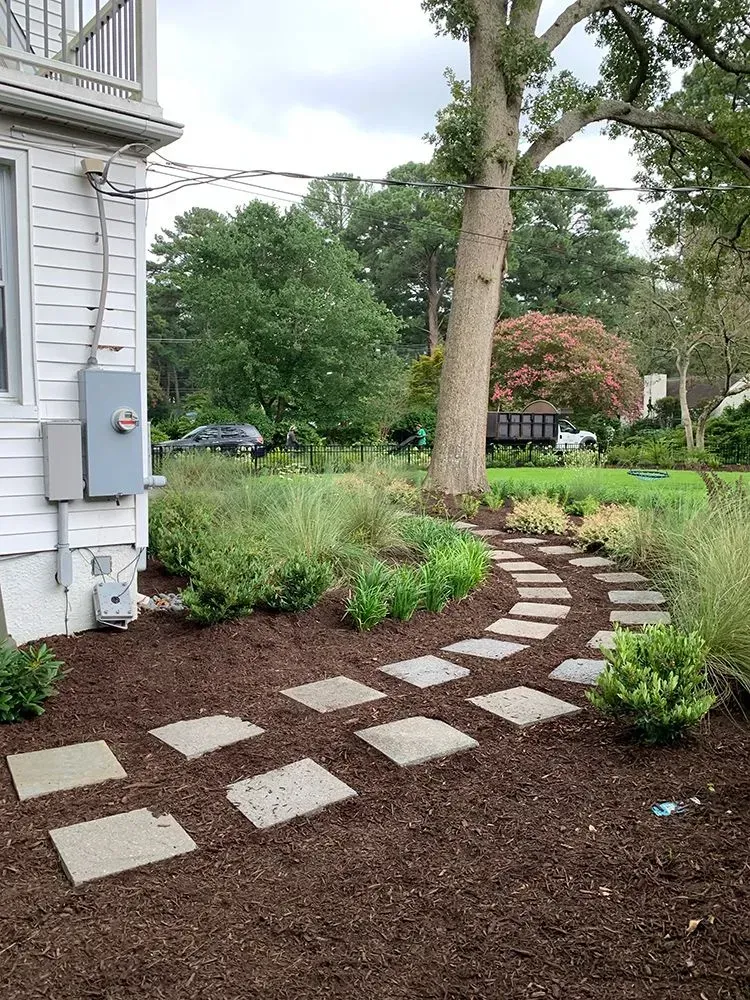 A stone walkway leading to a house in a garden.