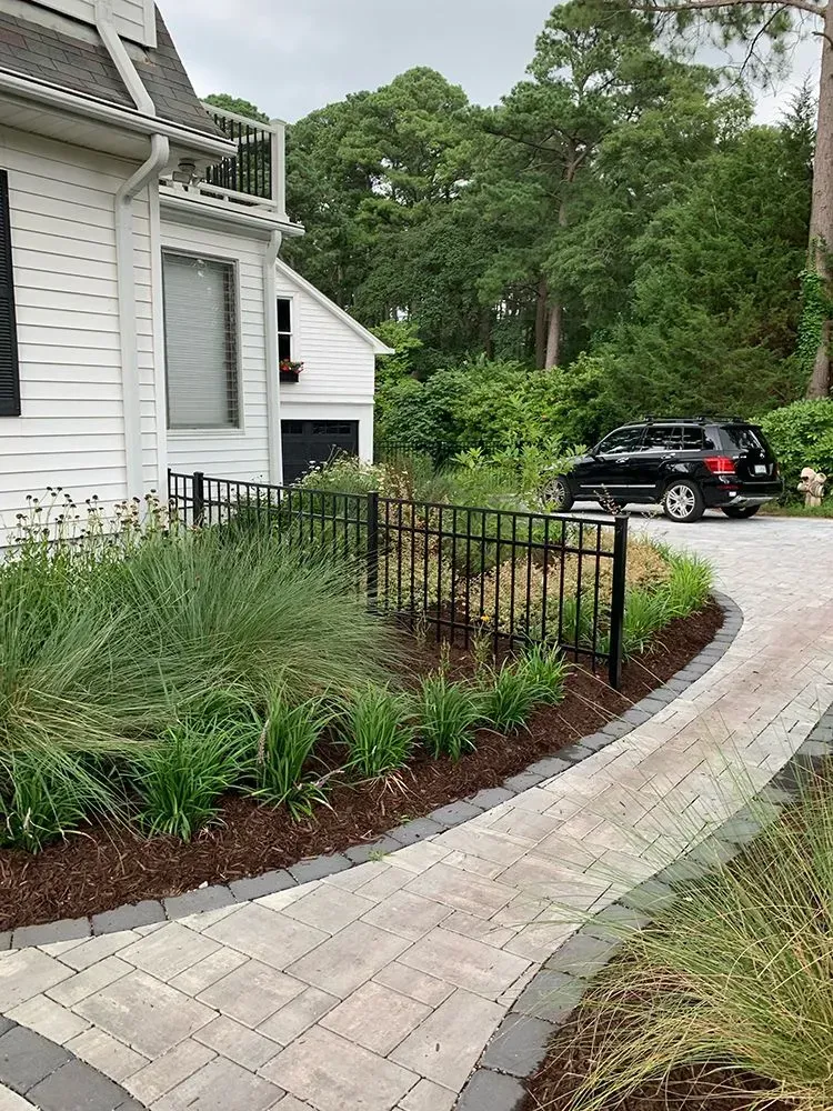 A brick walkway leading to a white house with a black suv parked in front of it.